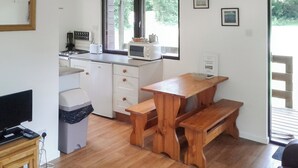 A compact kitchen with a microwave, toaster, and sink. There is a wooden bench and a small table. - 2 bedroom accommodation in North Tamerton, Bude (North Tamerton, Bude)