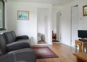 A living room with a sofa, a TV on a wooden stand, a framed picture on the wall, and a door leading to another room.