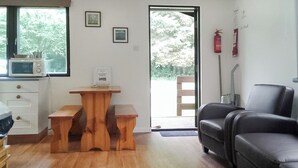 Un salon avec une table en bois, un canapé en cuir noir, un four à micro-ondes et une porte donnant sur l’extérieur.