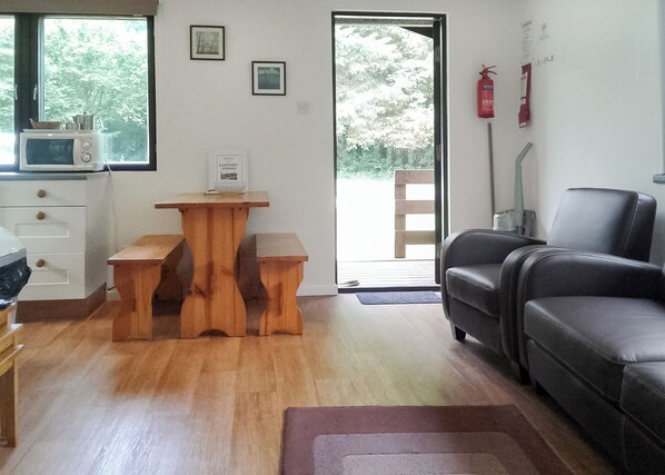 A living room with a wooden table, a black leather sofa, a microwave, and a door leading outside.