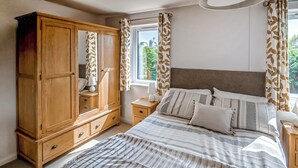 Un dormitorio con un armario grande de madera, una cama con ropa de cama a rayas y cortinas con estampado de hojas.