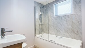 Un baño moderno con ducha envuelta en vidrio, lavamanos blanco y una bañera grande.