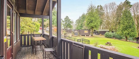 Terraza de madera con mobiliario exterior y vista a un área verde con árboles y cabañas.
