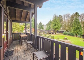 Terraza de madera con mobiliario exterior y vista a un área verde con árboles y cabañas.