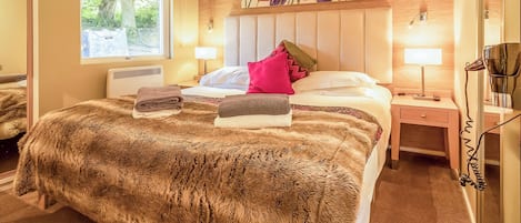 A hotel room with a large bed, a window with blinds, a painting of flowers on the wall, and a hairdryer on the nightstand.