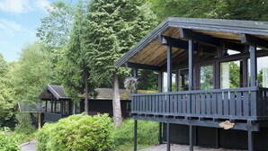 Una cabana de fusta amb un balcó, envoltada de vegetació abundant i arbres.