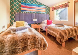Una habitación con dos camas, un cabecero, una ventana con cortina y una pared con diseño geométrico.