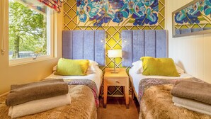 Habitació amb dos llits, una tauleta de nit, una finestra amb cortines i una paret decorada amb motius florals.