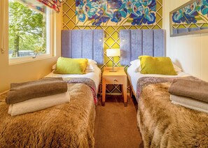 A room with two beds, a nightstand, a window with curtains, and a wall with floral artwork.