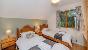 Een slaapkamer met twee houten bedden, een raam met gordijnen, een nachtkastje met een lamp en een radiator.