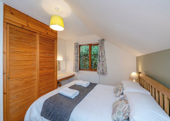 Ein Schlafzimmer mit Bett, Holzschrank, Fenster mit Vorhängen und einer Lampe.