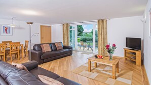 A modern living room with a leather sofa, a coffee table with fruit, a TV, and a view of the outdoors. - Ground floor apartment with one double, one twin and one with bunks. (Dawlish Warren)