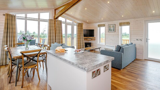 A spacious living area with a kitchen island, seating, and a television. - Field View Lodge (Pet) (Bretby, Derbyshire)