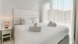 Una habitación de hotel con una cama grande, una mesita de noche con lámpara y cortinas translúcidas en la ventana.