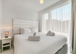 Ein Hotelzimmer mit einem großen Bett, einem Nachttisch mit Lampe und transparenten Vorhängen am Fenster.