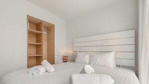 Quarto de hotel com uma cama grande, um guarda-roupa de madeira, uma mesa de cabeceira com uma lâmpada e uma cabeceira com linhas horizontais.