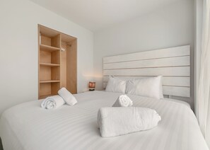 A hotel room with a large bed, a wooden wardrobe, a bedside table with a lamp, and a headboard with horizontal lines. - Sea Breeze Premier apartments are perfect for a getaway with friends. (Millendreath, Looe)