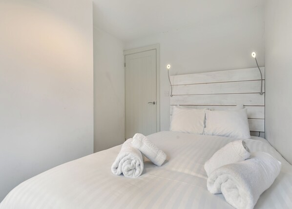 Un lit bien fait, avec du linge de lit blanc et des serviettes pliées, une tête de lit en bois et une porte blanche en arrière-plan.