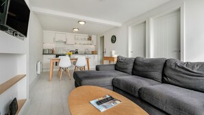 Una sala moderna con un sofá gris, una mesa de centro de madera y una cocina al fondo.