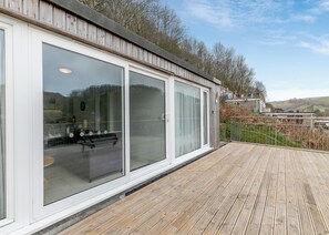 Un bâtiment moderne doté de grandes fenêtres en verre, d’une terrasse en bois et offrant une vue sur le paysage environnant.