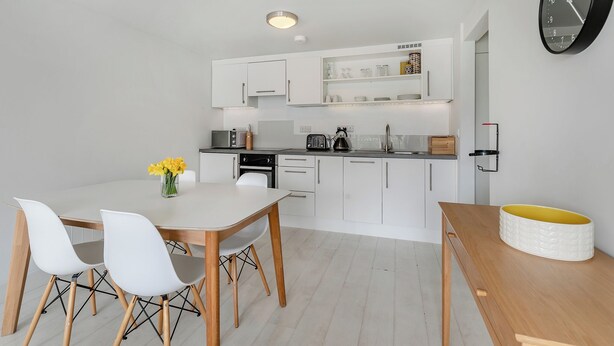 Uma cozinha moderna com armários brancos, uma mesa de jantar com cadeiras e um relógio na parede.