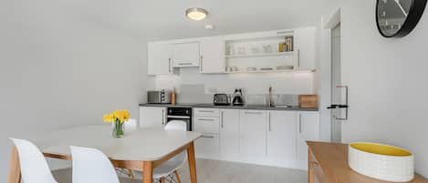 A modern kitchen with white cabinetry, a dining table with chairs, and a clock on the wall.