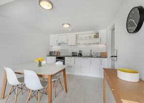 A modern kitchen with white cabinetry, a dining table with chairs, and a clock on the wall. - Sea Breeze Premier apartments are perfect for a getaway with friends. (Millendreath, Looe)