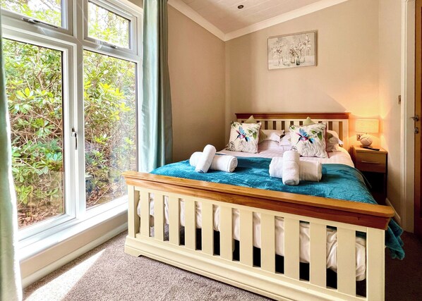 Une chambre à coucher avec un lit, une table de chevet, une lampe et une fenêtre donnant sur un paysage verdoyant.