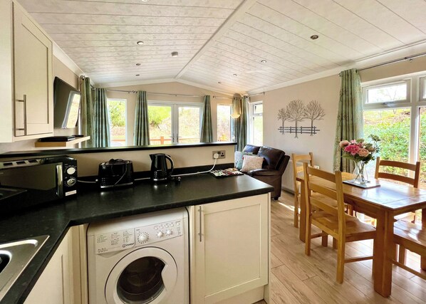 Een kleine keuken met een wasmachine, een koffiezetapparaat en een broodrooster. Er is een eethoek met een tafel en stoelen.