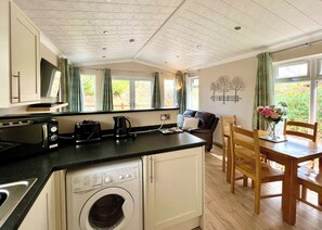 Een kleine keuken met een wasmachine, een koffiezetapparaat en een broodrooster. Er is een eethoek met een tafel en stoelen.