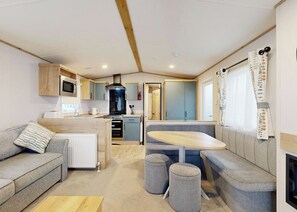 Eine kompakte Küchenzeile für Wohnmobile mit einer zentralen Kochinsel, einem Essbereich mit Sitzbank und einer Lounge-Ecke mit Hocker.
