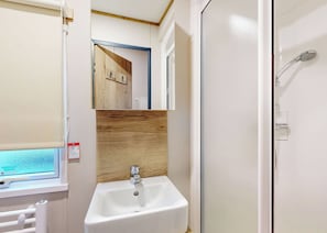 A bathroom with a white sink, wooden panel backsplash, a mirror, and a shower area.