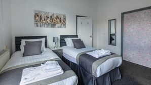Ein Hotelzimmer mit zwei Betten, einem Stadtbild, einem Spiegel und floralem Wandpapier.