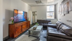 Ein modernes Wohnzimmer mit großem Flachbildfernseher, Ledersofa, Holzschrank und einem Glastisch.