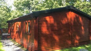 Una cabaña de madera roja con un porche, rodeada de árboles.