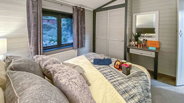 Un dormitorio con cama, ventana con cortinas, cómoda con artículos de aseo y espejo.