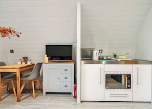 A compact kitchenette with a microwave, kettle, and coffee maker, a dining area with a wooden table and chairs, and a TV on a cabinet. - 0 bedroom accommodation in Pershore (Pershore)