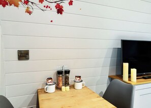 A modern room with a wooden table, a TV, and a wall-mounted light switch. - 0 bedroom accommodation in Pershore (Pershore)