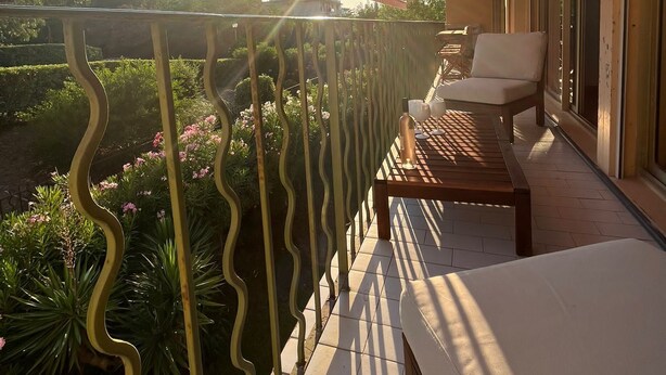 A balcony with a view of a garden and a building in the background.