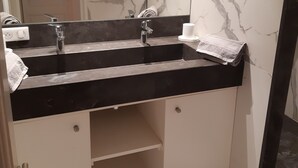 A bathroom with a black countertop, two sinks, a mirror, and marble walls.