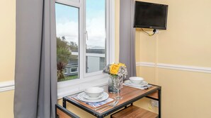 Un área de comedor con una mesa dispuesta para dos personas, una ventana con cortinas y un televisor de pantalla plana montado en la pared.