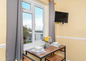 A dining area with a table set for two, a window with curtains, and a flat-screen TV mounted on the wall.