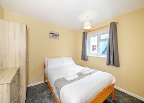 A bedroom with a bed, a wardrobe, a window with curtains, a small picture on the wall, and a ceiling light.