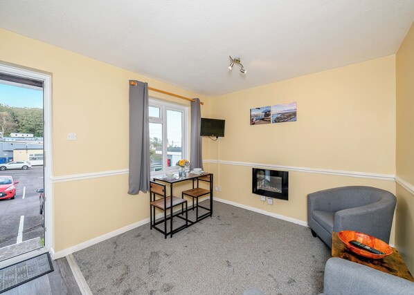 A room with a dining table, chairs, a TV, a sofa, and a view of a parking lot.