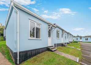 A row of light blue mobile homes with white trim, numbered windows, and a paved parking area.