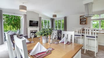 A modern dining room with a wooden table, white chairs, a television, and a fireplace.