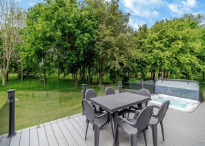 A deck with a table and chairs, a hot tub, and a view of a wooded area.