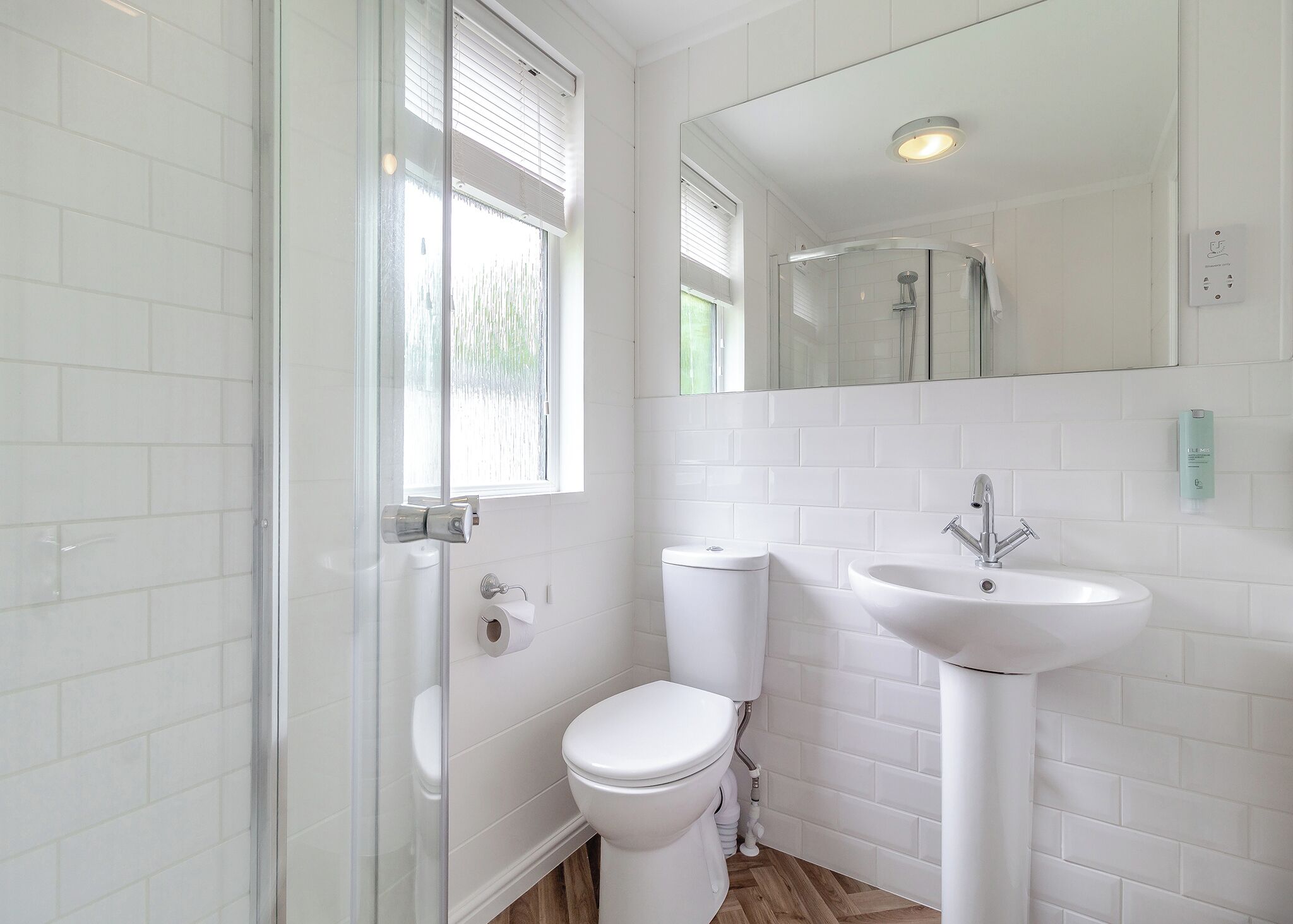 A bathroom with a toilet, a sink, a glass shower enclosure, and a window with blinds.