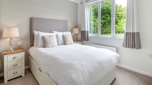 Un dormitorio con una cama grande, dos mesitas de noche, una ventana con cortinas y un radiador.