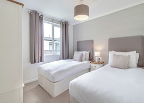 Habitación de hotel con dos camas, una ventana con cortinas, una mesita de noche con lámpara y un accesorio de iluminación en el techo.